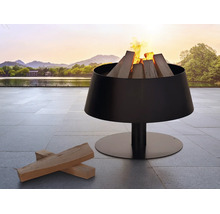 Moderne schwarze Feuerschale aus Metall mit brennendem Kaminholz auf einer Terrasse mit Steinplatten vor einem See und Bergen.
