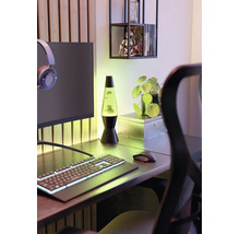 Une lampe à lave verte sur un bureau moderne avec un clavier d'ordinateur, une souris, un écran et une petite plante.