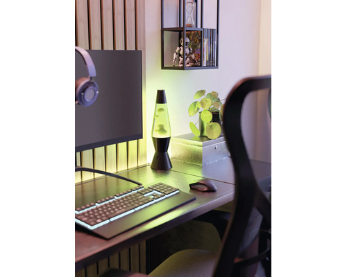 Une lampe à lave verte sur un bureau moderne avec un clavier d'ordinateur, une souris, un écran et une petite plante.