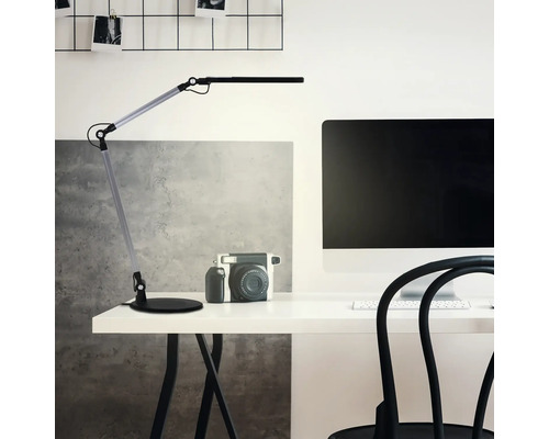 Verstellbare Schreibtischlampe an einem hellen Arbeitsplatz mit Schreibtisch, Monitor und Kamera.
