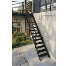 Schwarze Außentreppe aus Metall mit Geländer, führt zu einem Balkon, an einer Betonwand neben einer bepflanzten Gartenfläche.