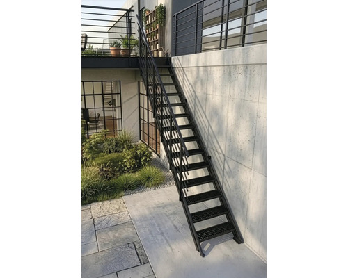 Schwarze Außentreppe aus Metall mit Geländer, führt zu einem Balkon, an einer Betonwand neben einer bepflanzten Gartenfläche.