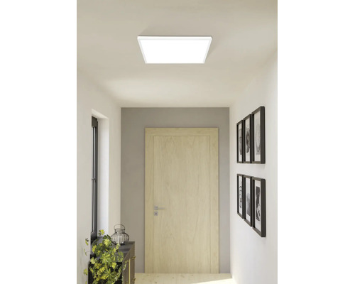 Panneau de plafond LED carré dans un couloir moderne et lumineux avec une porte en bois et des décorations murales.