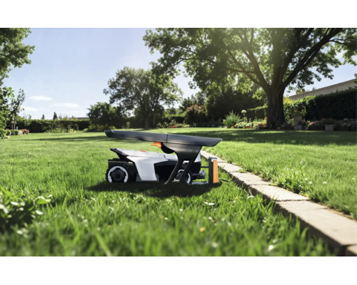 Robot tondeuse sous un abri sur une pelouse dans un jardin ensoleillé avec des arbres et une bordure en pierre.