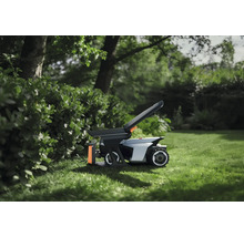 Robot tondeuse avec accessoires sur une pelouse dans le jardin à côté d'une haie.