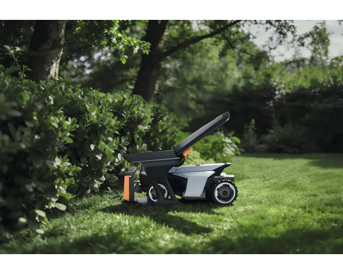Robot tondeuse avec accessoires sur une pelouse dans le jardin à côté d'une haie.
