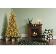 Festliches Wohnzimmer mit beleuchtetem goldenem Weihnachtsbaum, Kamin aus Holz und grünem Sessel mit karierter Decke.