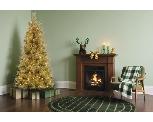 Festliches Wohnzimmer mit beleuchtetem goldenem Weihnachtsbaum, Kamin aus Holz und grünem Sessel mit karierter Decke.