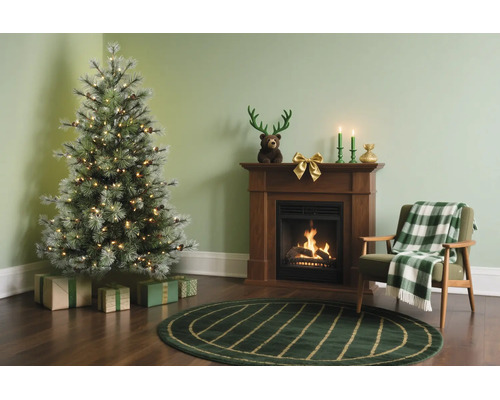 Festliches Wohnzimmer mit künstlichem Weihnachtsbaum, Kamin, Sessel mit Decke und Weihnachtsdekoration auf dunklem Holzboden.