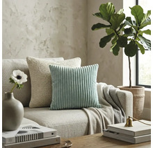 Modernes Wohnzimmer mit mintgrünem Cordkissen und beigem Strickkissen auf einem neutralen Stoffsofa.