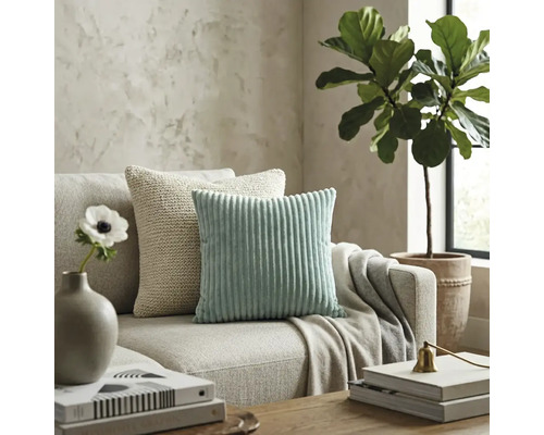 Modernes Wohnzimmer mit mintgrünem Cordkissen und beigem Strickkissen auf einem neutralen Stoffsofa.
