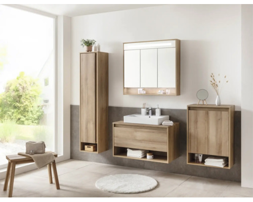 Salle de bains lumineuse avec meubles décor chêne, vasque blanche, armoire de toilette, colonne et meuble bas devant du carrelage gris.