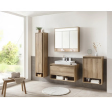 Salle de bains lumineuse avec meubles décor chêne, vasque blanche, armoire de toilette, colonne et meuble bas devant du carrelage gris.