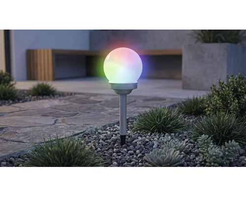 Solar-Kugelleuchte für den Garten mit mehrfarbiger RGB-Beleuchtung, auf einem Erdspieß in einem Kiesbeet mit Pflanzen.