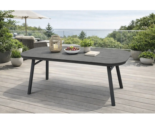 Moderner ovaler Gartentisch auf einer Terrasse mit Holzdeck. Der dunkle Tisch ist dekoriert mit einer Laterne, Obstschale und Pflanze.