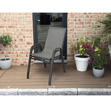 Stapelbarer Gartenstuhl mit Aluminiumgestell und Textilbespannung auf einer Terrasse mit Holzdeck und Pflanzen vor einer Ziegelwand.