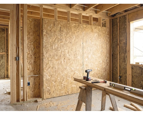Helle Rohbau Innenansicht mit OSB-Platten an Holzständerwänden, Dämmung und ordentlicher Werkbank mit Akkuschrauber, Hammer und Wasserwaage.