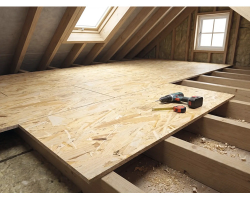 Dachstockausbau mit OSB-Platten auf Holzbalken, Akkuschrauber und Rollmeter auf der Verlegefläche im hellen Dachraum.