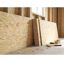 OSB-Platten an einer Holzwand in einem hellen Rohbau mit Hammer, Massband und Schrauben auf dem Boden.