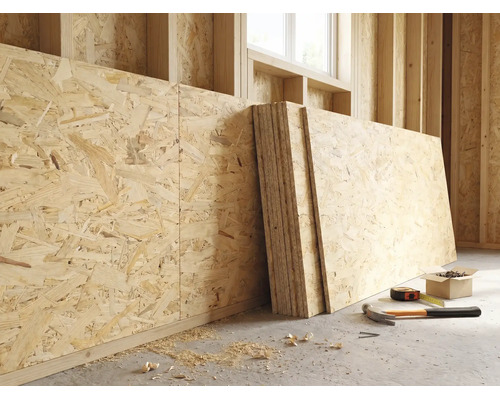 OSB-Platten an einer Holzwand in einem hellen Rohbau mit Hammer, Massband und Schrauben auf dem Boden.