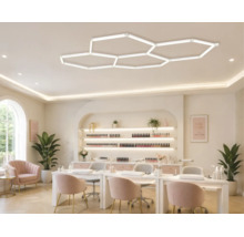 Moderne LED-Deckenleuchte in Wabenform in einem hellen, gut organisierten Nagelstudio mit Manikürtischen und Samtstühlen.