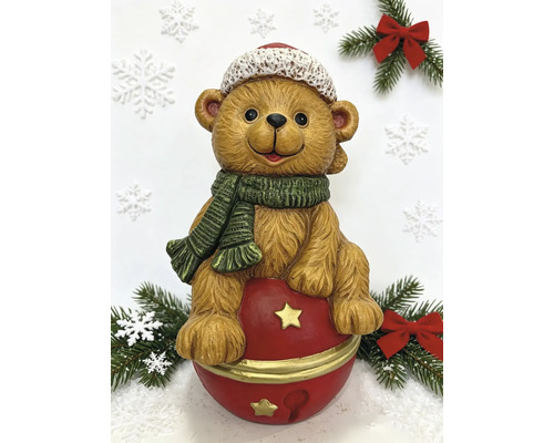 Weihnachtsfigur Teddybär auf einer Glocke mit Mütze und Schal zwischen Tannenzweigen und Schneeflocken.