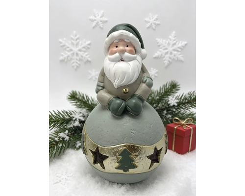 Figurine de Père Noël sur une boule avec découpes d'étoiles et de sapin, branches de sapin et cadeau en arrière-plan.