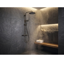 Modernes Badezimmer mit schwarzer Regendusche, dunklen Schieferwänden, Holzbank mit weißen Handtüchern und Wasserdampf.