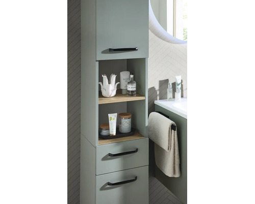 Meuble de salle de bain moderne vert sauge avec étagères ouvertes en bois, tiroirs et poignées noires dans une salle de bain lumineuse.
