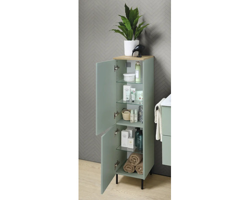 Armoire latérale de salle de bain organisée en vert clair avec portes ouvertes, étagères en verre, plateau décor bois et pieds noirs.