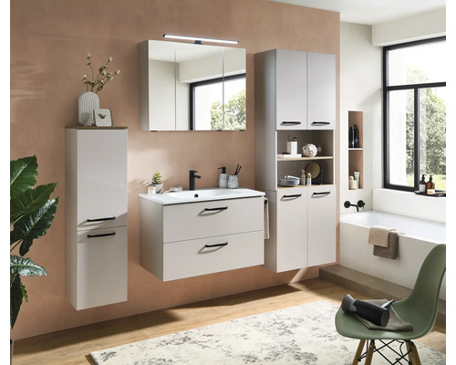 Ensemble de meubles de salle de bains moderne gris clair avec sous-vasque, armoire de toilette éclairée et colonnes dans une pièce lumineuse.