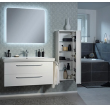 Salle de bains moderne avec meuble sous-lavabo blanc, miroir éclairé et armoire haute ouverte avec étagères en verre devant un mur tapissé.