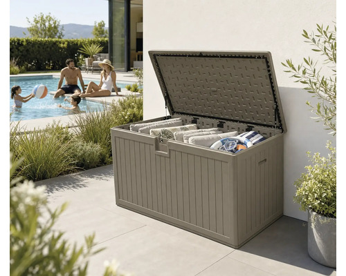Coffre de jardin ouvert en plastique aspect bois, rempli de coussins et d'accessoires de piscine sur une terrasse à côté d'une piscine.