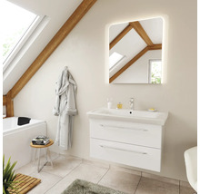 Salle de bains lumineuse sous les combles avec poutres en bois, meuble sous-vasque blanc, lavabo céramique, miroir LED carré et baignoire.