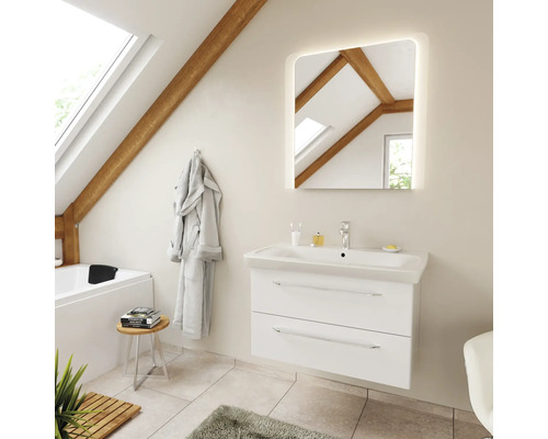 Salle de bains lumineuse sous les combles avec poutres en bois, meuble sous-vasque blanc, lavabo céramique, miroir LED carré et baignoire.