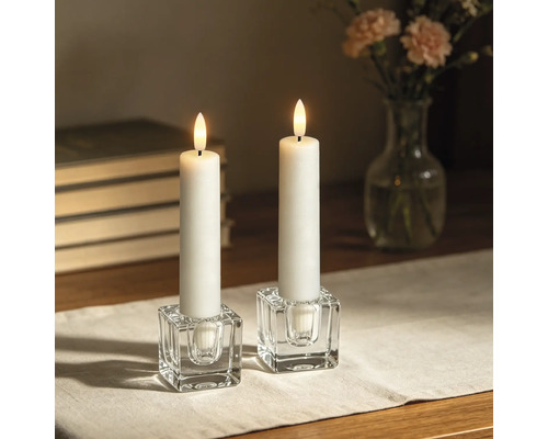 Deux bougies LED blanches dans des bougeoirs en verre transparent en forme de cube sur une table.