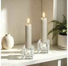 Deux bougies LED dans des bougeoirs en verre cubiques sur une étagère lumineuse et organisée avec un vase et une plante.