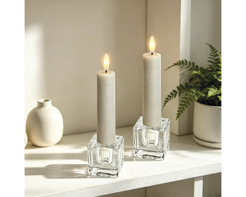 Deux bougies LED dans des bougeoirs en verre cubiques sur une étagère lumineuse et organisée avec un vase et une plante.