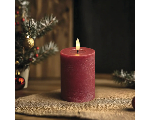 LED-Stumpenkerze mit rustikaler Oberfläche und künstlicher Flamme in einer hellen und weihnachtlichen Dekoration mit Tannenzweigen.