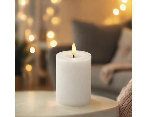 Weisse LED-Stumpenkerze auf einem Tisch vor einem unscharfen Hintergrund mit warmen Lichtern.