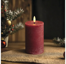 Rote LED-Stumpenkerze mit rustikaler Oberfläche vor einem weihnachtlichen Hintergrund.