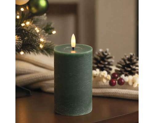 Bougie pilier LED avec surface texturée et flamme vacillante dans un décor de Noël avec sapin et pommes de pin.