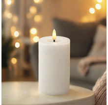 Bougie LED blanche avec ampoule en forme de flamme sur une table dans une pièce chaleureuse.