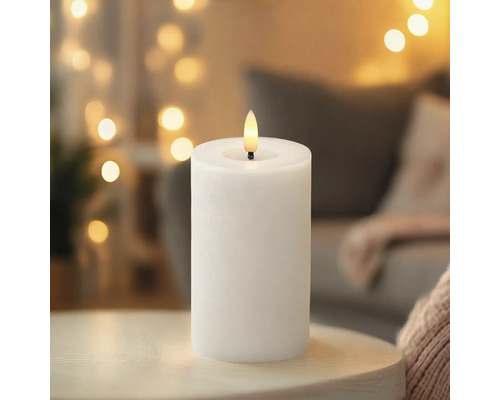 Bougie LED blanche avec ampoule en forme de flamme sur une table dans une pièce chaleureuse.
