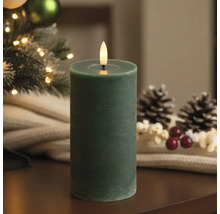 Bougie LED cylindrique verte aspect cire avec flamme vacillante dans un décor de Noël avec pommes de pin.