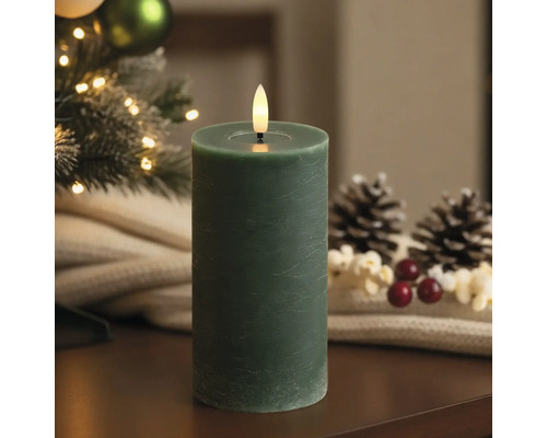 Bougie LED cylindrique verte aspect cire avec flamme vacillante dans un décor de Noël avec pommes de pin.