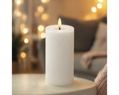 Bougie LED pilier blanche avec une flamme réaliste sur une surface en bois devant un arrière-plan de lumières floues.