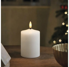 Weiße LED Stumpenkerze mit künstlicher Flamme auf einem Holztisch in weihnachtlicher Umgebung.