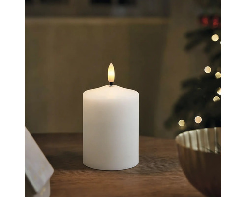 Weiße LED Stumpenkerze mit künstlicher Flamme auf einem Holztisch in weihnachtlicher Umgebung.