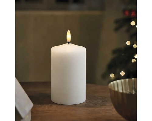 Weiße LED-Stumpenkerze auf einem Holztisch in einer weihnachtlich dekorierten Umgebung.